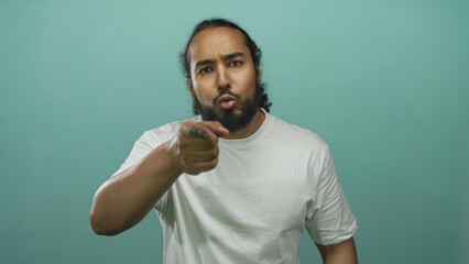 Man points finger directly toward camera in studio against teal backdrop, wearing a plain white t...