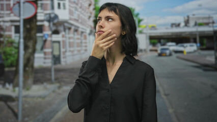 Woman in black shirt points finger to side on street with brick building facade and parked cars; denial.