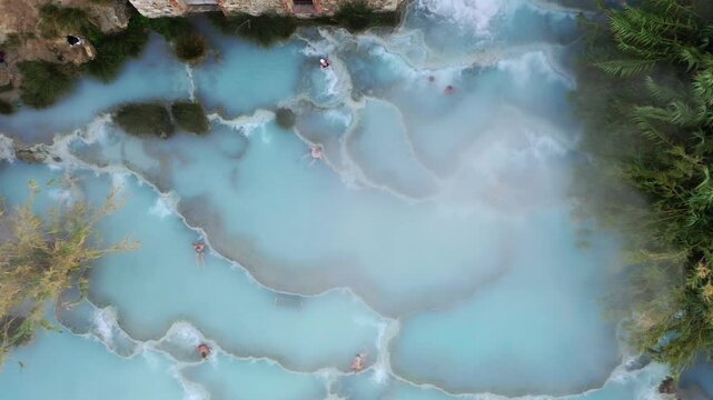 Toscana, Italy - 19 October 2025: Aerial view of the Saturnia thermal springs cascade, its milky blue waters contrasting with the green vegetation and red roof.