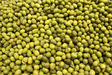 Green olives cracked for curing and brining, glossy surface and full-frame pattern; for food design, retail promotion, agriculture stories, education.