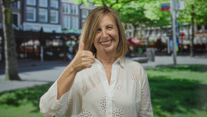 Fototapeta premium Middle age caucasian woman smiling and giving thumbs up gesture on sunlit street; optimism confidence.