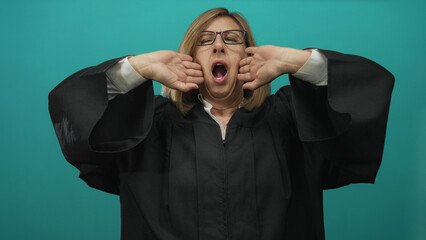 Middle age caucasian judge wearing black robe yawns with raised arms and open mouth against teal studio wall; fatigue.