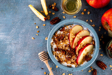 Healthy autumn breakfast or snack, bowl with Greek yogurt, granola, apples, honey and pecans, on blue concrete background with ingredient, copy space