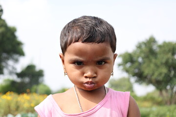 A captivating close-up portrait of a young Indian girl looking directly into the camera with an innocent and expressive face. The shallow depth of field creates a soft, natural outdoor background, bea