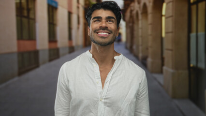 Obraz premium Man smiling showing teeth while looking up on historic sunlit street; optimism curiosity adventure inspiration.