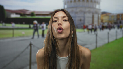 Obraz premium Young hispanic woman puckers lips gesture at tower in building near historic pisa site; playful flirtation.