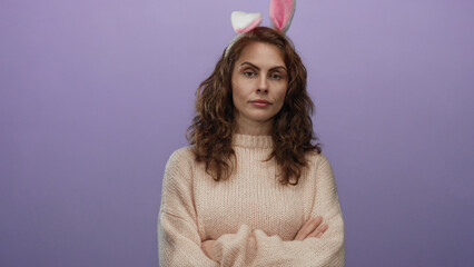 Woman wearing bunny ears stands over isolated purple background with folded arms and neutral expression, capturing a playful yet reserved mood with a soft knit sweater.