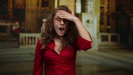 Woman surprised inside church with curly hair wearing glasses and red shirt with flag in background displaying shocked emotion indoors