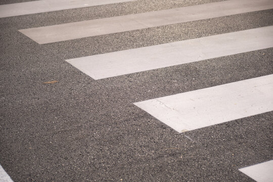Close-up of a pedestrian crosswalk showing white zebra stripes painted on textured asphalt, highlighting road surface details, contrast, and urban street safety and minimal composition.