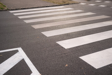 White striped pedestrian crosswalk on dark asphalt, showing bold zebra markings across a street near a sidewalk, highlighting urban road design, traffic control and pedestrian safety measures.