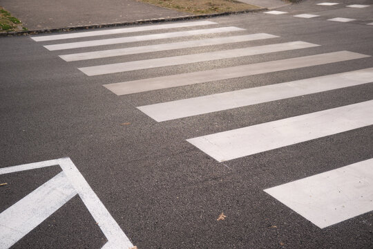 White striped pedestrian crosswalk on dark asphalt, showing bold zebra markings across a street near a sidewalk, highlighting urban road design, traffic control and pedestrian safety measures. - Powered by Adobe
