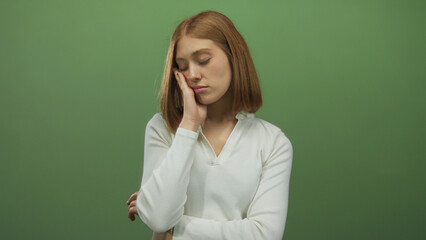 Woman appears contemplative against a solid green background, wearing a white shirt, with closed eyes portraying thoughtfulness and serenity.