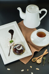 A tempting chocolate dessert on a plate, a cup of tea, and a teapot arranged elegantly