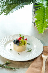 A delicious and colorful fruit tart on a decorative white plate, garnished with fresh herbs and a wooden spoon, creating a visually appealing still-life scene.