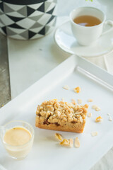 A delightful composition featuring a piece of crumble cake and tea. Beside the cake, a small glass with sauce, creating a tasty and visual pleasing scene