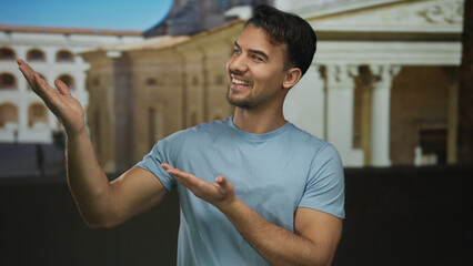 Obraz premium Young hispanic man extends hands outdoors, presenting in front of historic architecture with a joyful expression, capturing a dynamic moment in a vibrant setting.