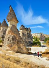 View of scenic geological formations and fairy chimneys. Woman stands on a winding white trail,...