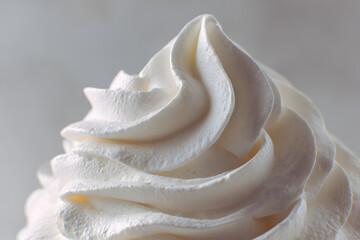 Close-up macro of fluffy whipped cream swirl on cake, textured with air bubbles, soft natural light highlighting freshness and smoothness, clean minimal background.
