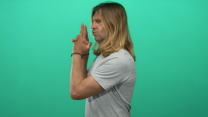 Man with long blond hair pointing finger like gun with stern puckered lips in green studio; playful...