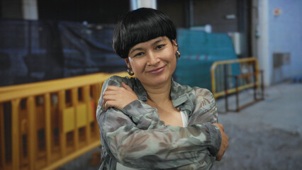 Woman embracing herself confidently in an urban construction site, showcasing strength against an industrial backdrop, blending personal serenity with the bustling environment.
