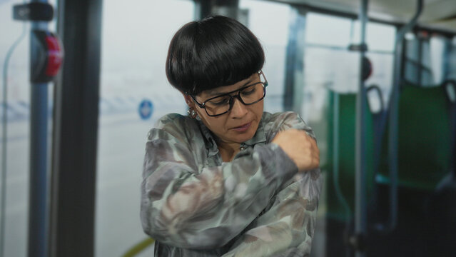 Woman feeling cold inside a bus while wearing glasses and a patterned jacket, showcasing discomfort in a public transport setting.