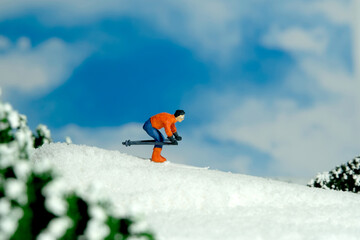 Miniature people toy figure photography. Winter sport. A male downhill ski racer slides down from the top of the hill.