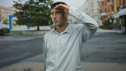 Man shielding eyes under sunlight on street corner amid city building facades; hope aspiration curiosity.