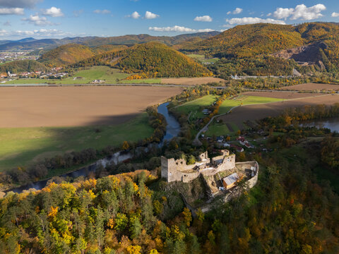 Aerial view of the stark, weathered ruins of Reviste Castle perched atop a vibrant, forested hill overlooking the meandering Hron River, Zarnovica, Banskobystricky kraj, Slovakia.