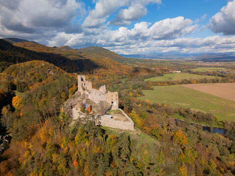 Aerial view of the stark grey ruins of Reviste Castle stand proudly amidst the vibrant tapestry of autumn foliage, Zarnovica, Banskobystricky kraj, Slovakia.