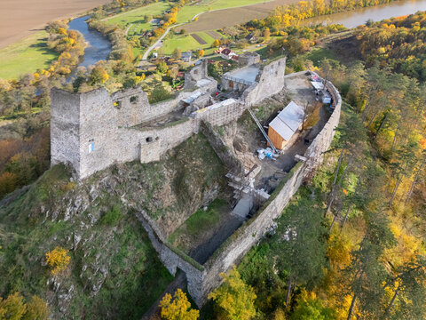 Aerial view of the stark stone ruins of Reviste Castle contrast with the vibrant autumn foliage, overlooking the winding river, Zarnovica, Banskobystricky kraj, Slovakia.