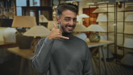 Obraz premium Man shows call gesture with finger to ear among beige lamps in modern building; welcoming communication.