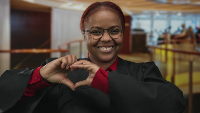 Woman judge in black robe shapes a heart with hands in hotel building lobby for supportive gesture; love.