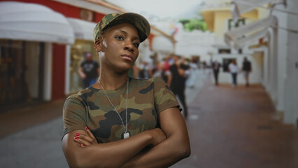 Woman soldier confidently crosses arms on busy city street wearing camouflage uniform and dogtags;...