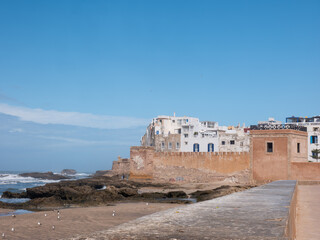 Historic Essaouira Medina Walls and Coastal Landscape with Rolling Atlantic Waves, Rocky Shore, and Seagulls under a Clear Blue Sky