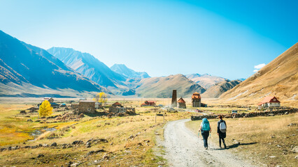 Obraz premium Hikers approaching the remote women’s monastery in Truso Valley, Georgia, with majestic mountains and autumn colors in the background