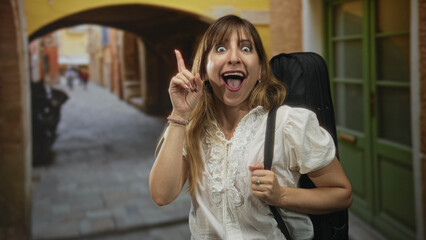 Woman pointing finger on narrow street carrying guitar case strap over shoulder; excitement travel music.