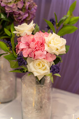 Beautiful bouquet featuring pink hydrangeas and white roses arranged in a clear glass vase on a table. The background features elegant purple drapery, enhancing the floral display's charm.