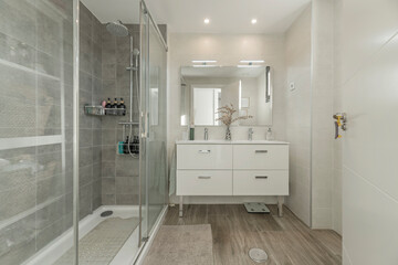 Modern minimalist bathroom with a floor-to-ceiling shower enclosure, wall-mounted cabinet, and a mirror with integrated LED lighting.