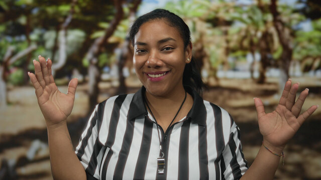 Referee in black and white striped shirt raises both palms to signal a decision during a match in forest clearing; fair play.