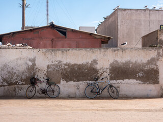 Coastal Street Scene in Essaouira, Morocco: Bicycles Leaning Against a Weathered Wall, with Seagulls and Unique Cell Towers