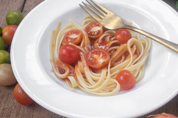 A minimalist plate of spaghetti pasta served with fresh cherry tomatoes on a rustic wooden table. Captured in warm natural sunlight with dramatic shadows, this still life food photograph.