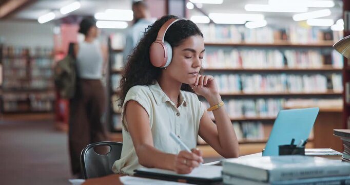 Student, laptop and writing in library with woman for education, assignment or thesis on college campus. Headphones, tech and female person with podcast, preparation for exam or research for paper