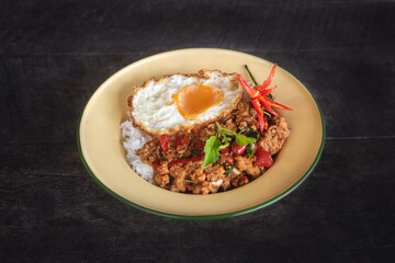 Beautifully presented stir-fried pork with basil and a fried egg, served in a vintage style plate garnished with fresh chilies, cucumber and herbs.