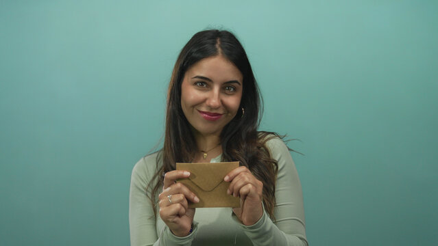Young hispanic woman holding envelope against an isolated green background wall, smiling and creating a cheerful atmosphere. - Powered by Adobe
