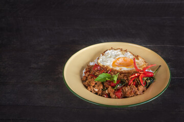Beautifully presented stir-fried pork with basil and a fried egg, served in a vintage style plate garnished with fresh chilies, cucumber and herbs.