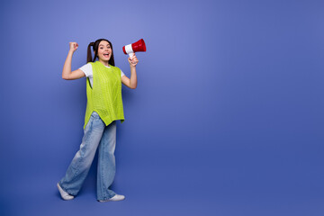 Young girl with neon green sweater and jeans holding a megaphone smiles confidently against a blue...