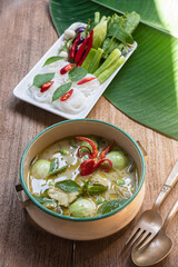Authentic Thai green curry with tender chicken and eggplants served with rice noodles and fresh vegetables. Traditional Thai food still life on wooden table, beautifully arranged with basil leave.