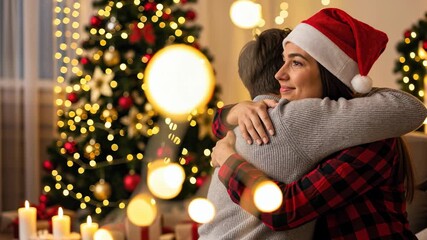 Happy couple hugging at home celebrating christmas day with lights and decorated tree.