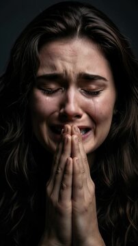 Woman praying in tears showing sadness grief and emotional distress in dark background.