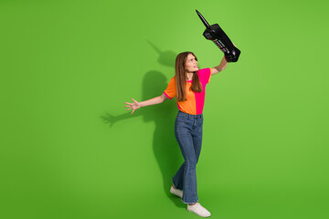 Young woman in colorful shirt and jeans holds a large toy phone against a green background for creative advertising